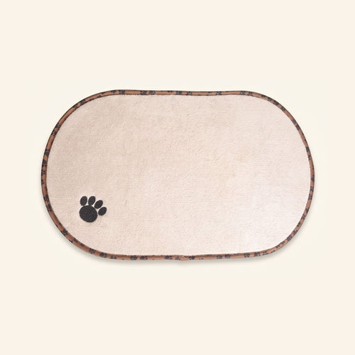 An oval beige pet feeding mat with a black paw print and a patterned brown border.