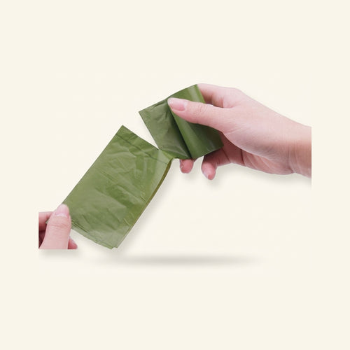 Green biodegradable dog poop bag being pulled from a roll by hand